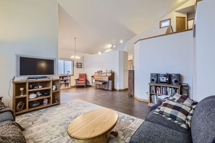 Cozy living room with a TV, bookshelf, and piano, featuring warm lighting and a soft rug.