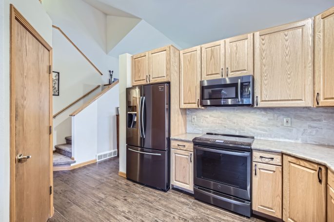 Modern kitchen featuring wooden cabinets, black appliances, and a staircase in the background.