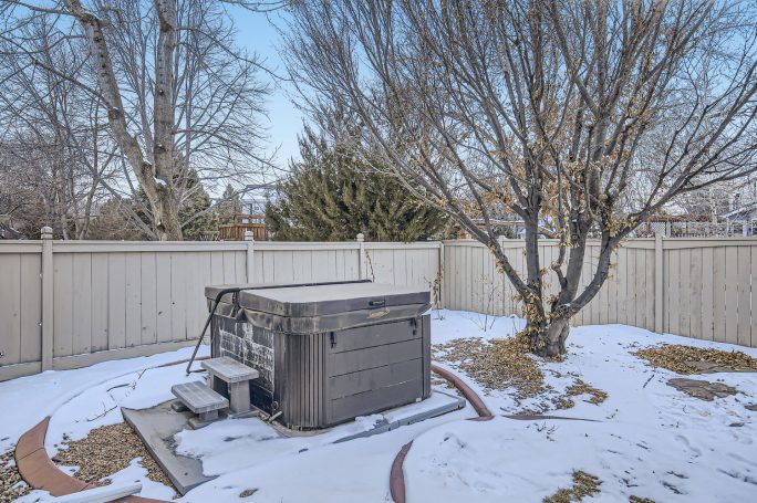 Hot tub in a snow-covered yard with a fence and bare trees.